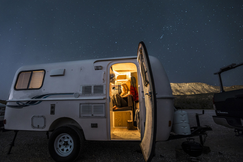 Woman sitting in illuminated camper trailer against star field stock photo