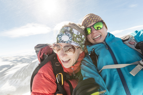 Glückliche Freundinnen mit Sonnenbrille und warmer Kleidung gegen den Himmel, lizenzfreies Stockfoto