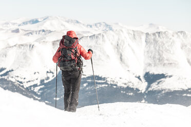 Rear view of female hiker with backpack holding hiking poles while standing against snowcapped mountains - CAVF27397