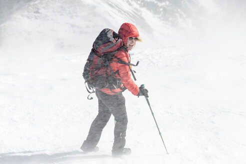 High angle view of female hiker with backpack holding hiking poles during snowstorm - CAVF27398