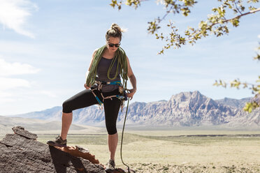 Frau in voller Länge beim Anziehen des Sicherheitsgeschirrs, während sie an den Bergen im Red Rock Canyon National Conservation Area steht - CAVF27415