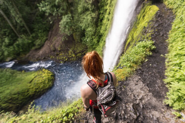 Hochformatige Ansicht einer Wanderin mit Rucksack, die auf dem Eagle Creek Trail vor den Tunnel Falls steht - CAVF27420