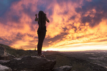 Unbeschwerte Frau in voller Länge auf einem Felsen stehend gegen einen dramatischen Himmel im South Mountain Park - CAVF27422