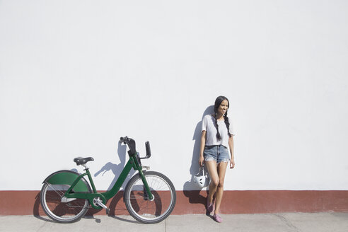 Happy woman holding helmet while standing by bicycle on sidewalk - CAVF27452