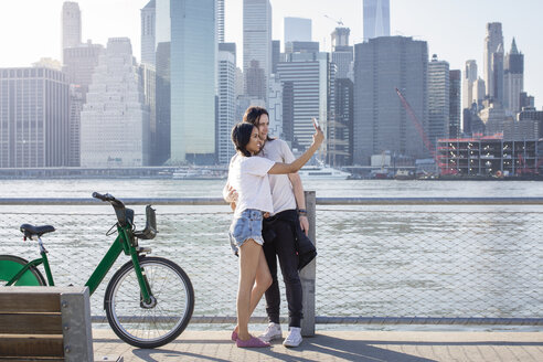 Paar, das Selfie auf dem Handy, während stehend von Fahrrädern gegen Stadtbild - CAVF27458