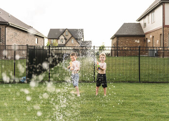 Portrait of boys squirting with water gun in backyard - CAVF27501