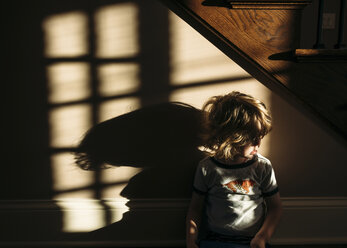 Boy sitting in beneath staircase at home - CAVF27512