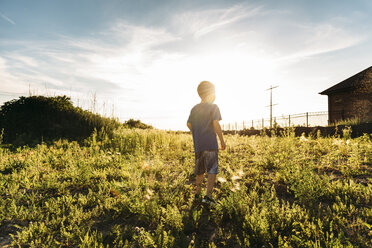 Rear view of boy standing on grassy field against sky - CAVF27527