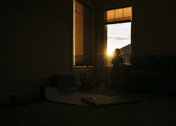 Silhouette eines Jungen, der durch das Fenster seines Hauses schaut - CAVF27528