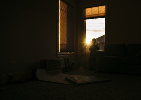 Silhouette of boy looking through window at home - CAVF27528