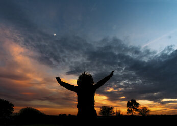 Silhouette eines fröhlichen Jungen mit erhobenen Armen, der vor einem bewölkten Himmel steht - CAVF27542