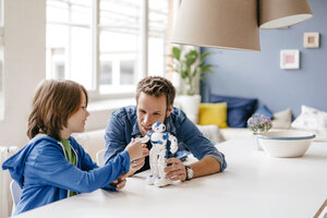 Glücklicher Vater und Sohn spielen mit einem Roboter auf dem Tisch zu Hause - KNSF03581