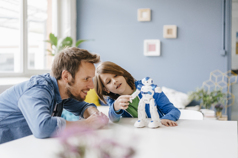 Glücklicher Vater und Sohn spielen mit einem Roboter auf dem Tisch zu Hause, lizenzfreies Stockfoto