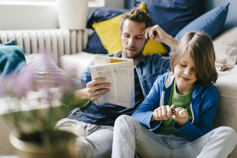 Vater liest Zeitung, während der Sohn zu Hause schnitzt, lizenzfreies Stockfoto