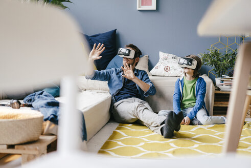 Father and son wearing VR glasses sitting on the floor at home - KNSF03596