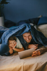 Happy father and son watching a movie on tablet under blanket - KNSF03605