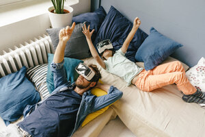 Father and son wearing VR glasses lying down at home - KNSF03609