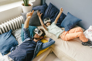 Vater und Sohn mit VR-Brille im Liegen zu Hause - KNSF03609
