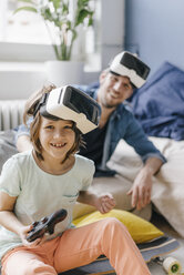 Portrait of happy boy and father wearing VR glasses playing video game at home - KNSF03613
