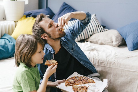 Father and son eating pizza at home stock photo