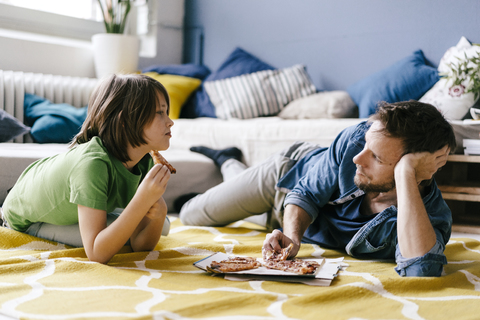 Father and son eating pizza on the floor at home stock photo