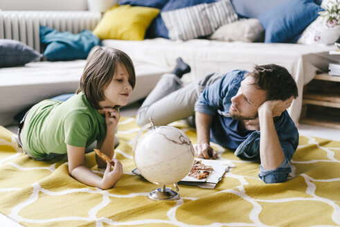 Vater und Sohn essen Pizza neben dem Globus auf dem Boden zu Hause - KNSF03621