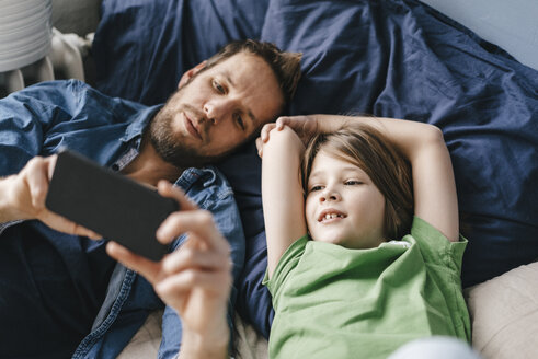 Vater und Sohn schauen zu Hause gemeinsam auf ihr Smartphone - KNSF03631