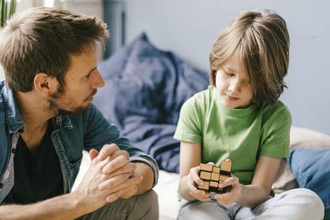 Father looking at son playing with cube a at home stock photo