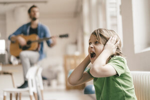 Verängstigter Sohn hält sich die Ohren zu, wenn sein Vater zu Hause Gitarre spielt - KNSF03636