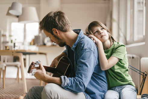 Son leaning against father playing guitar at home - KNSF03637