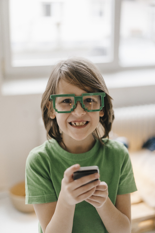 Porträt eines lächelnden Jungen mit Pixelbrille, der ein Mobiltelefon hält, lizenzfreies Stockfoto
