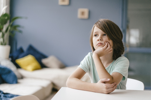 Porträt eines traurigen Jungen, der zu Hause am Tisch sitzt, lizenzfreies Stockfoto