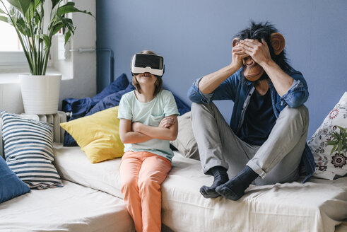 Vater mit Affenmaske sitzt zu Hause neben seinem Sohn mit VR-Brille - KNSF03648