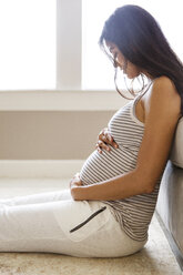 Seitenansicht einer lächelnden schwangeren Frau, die zu Hause auf dem Sofa sitzt - CAVF27543