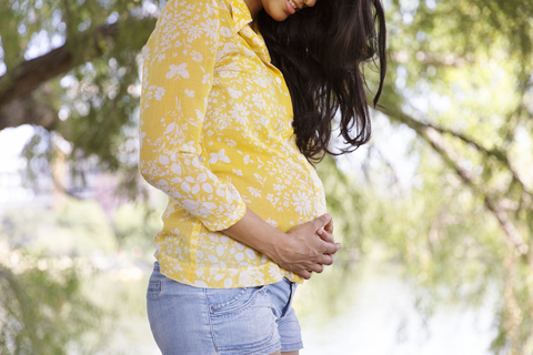 Midsection der schwangeren Frau mit Händen auf dem Bauch stehend im Park, lizenzfreies Stockfoto