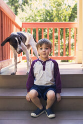 Porträt eines Jungen, der an einem sonnigen Tag mit einem Hund auf den Stufen sitzt - CAVF27564