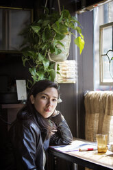Porträt einer jungen Frau, die am Tisch am Fenster sitzt - CAVF27572