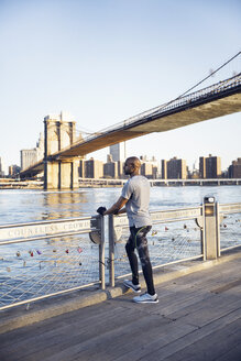 Männlicher Athlet in voller Länge auf der Promenade stehend mit der Brooklyn Bridge im Hintergrund - CAVF27579