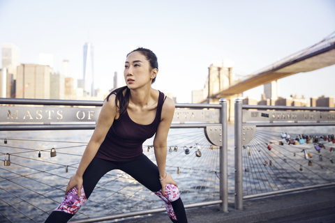 Nachdenkliche Sportlerin beim Training auf der Promenade mit Brooklyn Bridge und One World Trade Center im Hintergrund, lizenzfreies Stockfoto