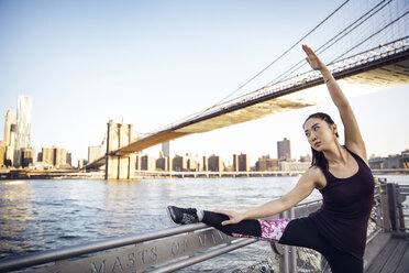 Weibliche Athletin streckt Bein und Arm auf der Promenade mit der Brooklyn Bridge im Hintergrund - CAVF27587