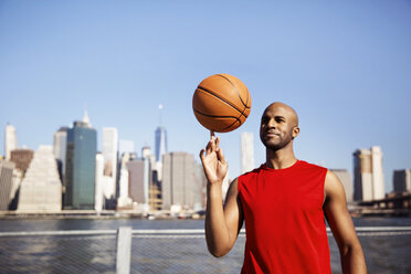 Lächelnder Mann, der einen Basketball auf dem Finger vor der Skyline der Stadt dreht - CAVF27592