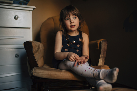 Mädchen schaut weg, während sie zu Hause auf einem Sessel sitzt, lizenzfreies Stockfoto