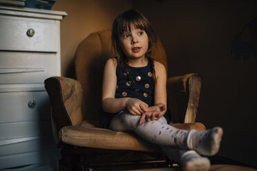 Girl looking away while sitting on armchair at home - CAVF27609