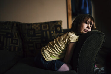 Bored girl looking away while kneeling on sofa - CAVF27615