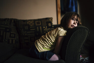 Gelangweiltes Mädchen, das auf dem Sofa kniend wegschaut - CAVF27615