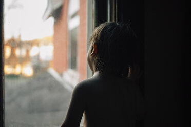 Rückansicht eines Jungen ohne Hemd, der durch ein Fenster schaut - CAVF27616