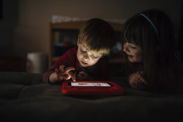 Happy siblings playing video game while lying on bed at home - CAVF27622