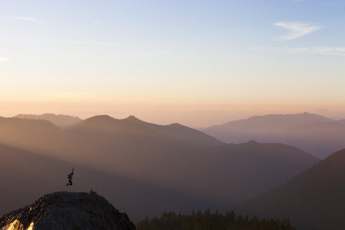 Frau springt bei Sonnenuntergang auf eine Felsformation gegen den Himmel - CAVF27633