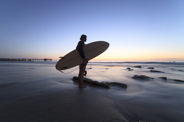 Frau hält Surfbrett, während sie am Ufer gegen den klaren Himmel steht - CAVF27642