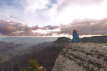 Rückansicht einer auf einem Felsen sitzenden Frau mit Blick auf die Berge bei bewölktem Himmel - CAVF27643